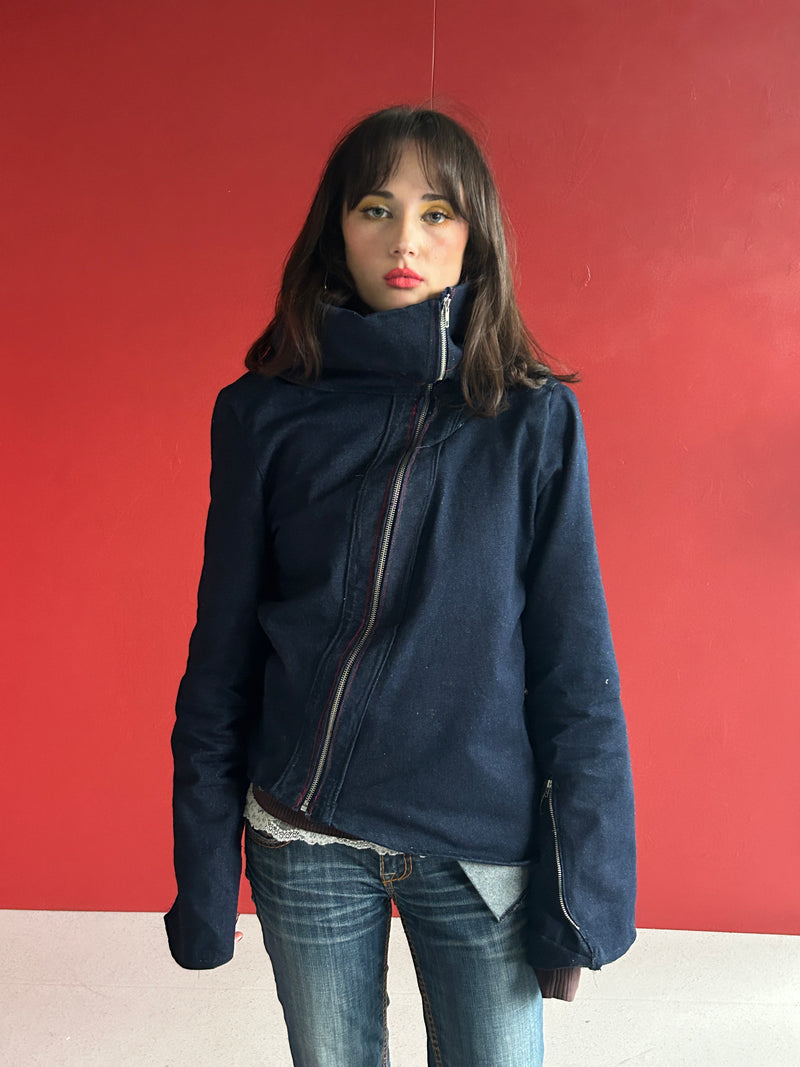 Person wearing a blue jacket and jeans standing against a red wall.