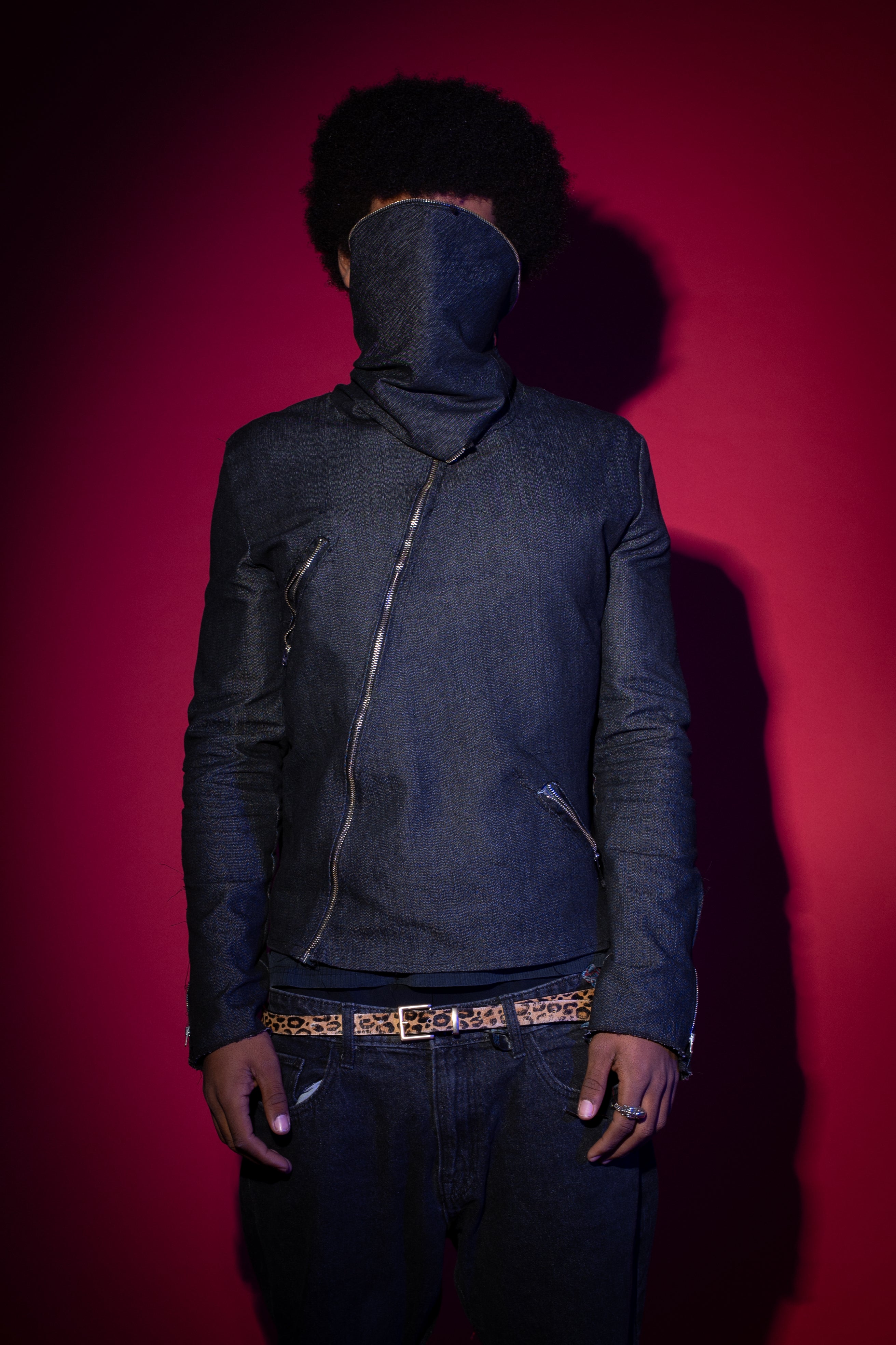 Person wearing a dark jacket and pants with a hood against a red background